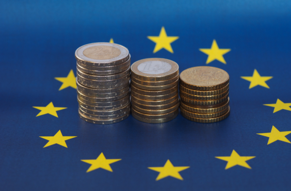 Zdjęcie prezentujące flagę Unii Europejskiej i stosy monet