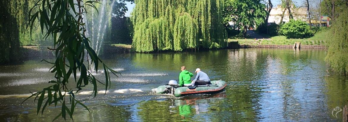 Na zdjęciu widać mężczyzn płynących na łódce w stawie w Parku Traugutta