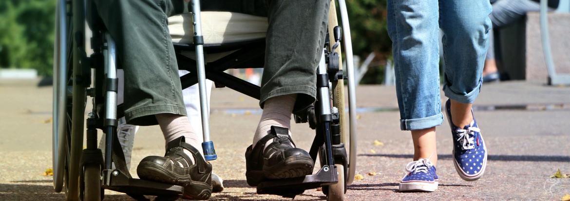 Osoba niepełnosprawna jadąca na wózku obowk spacerującego opiekuna