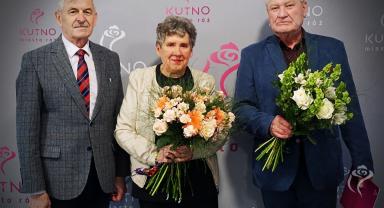 Na zdjęciu widać trzy osoby, dwie trzymają kwiaty