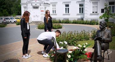 Na zdjęciu widać trzy osoby składające kwiaty