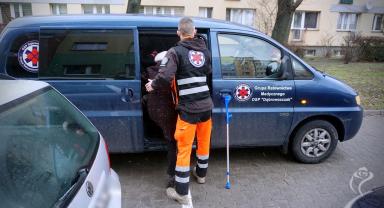Na zdjęciu widać wolontariusza, który pomaga starszej kobiecie wsiąść do samochodu