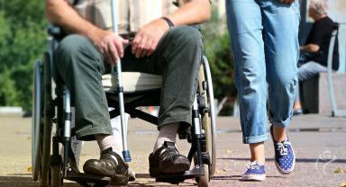 Osoba niepełnosprawna jadąca na wózku obowk spacerującego opiekuna