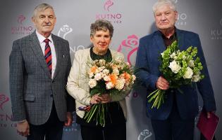 Na zdjęciu widać trzy osoby, dwie trzymają kwiaty