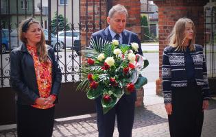 Na zdjęciu widać trzy osoby niosące kwiaty