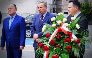 Na zdjęciu widać trzy osoby, jedna trzyma kwiaty