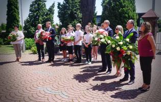 Na zdjęciu widać kilkanaście osób, niektóre z nich trzymają kwiaty