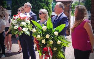 Na zdjęciu widać kilka osób, niektóre z nich trzymają kwiaty